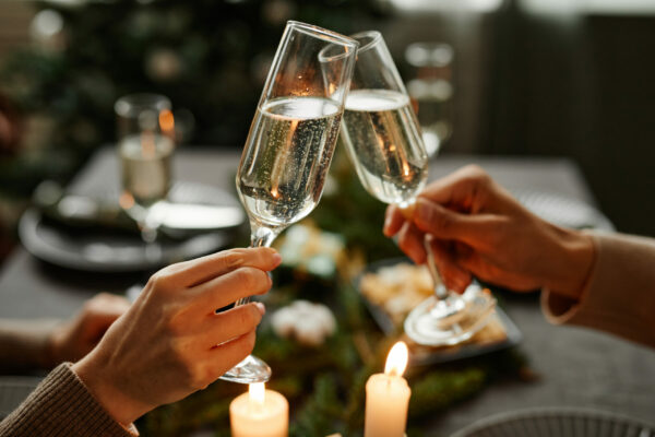 Side view close up of young couple clinking champagne glasses while enjoying Christmas dinner together sitting by elegant dining table with candles