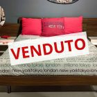 Letto Matrimoniale con testata a muro formata da due pannelli sovrapposti di altezze differenti con la scritta: "Venduto" sopra.